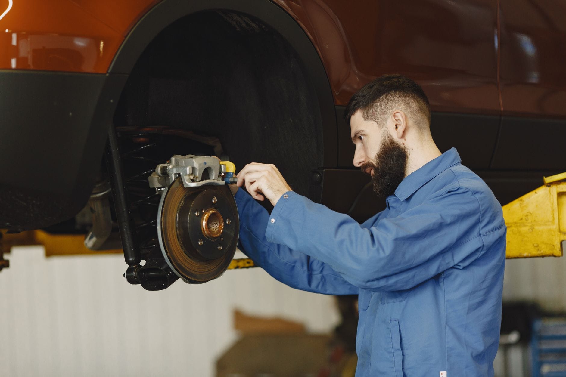 Mechanik w niebieskim kombinezonie naprawia hamulce pojazdu w warsztacie